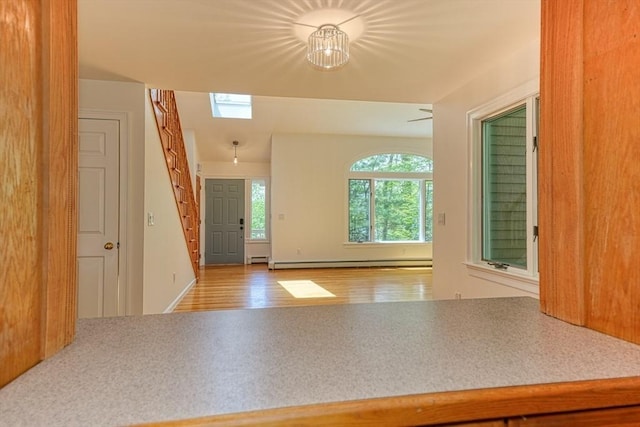 foyer featuring baseboard heating, stairs, wood finished floors, and a skylight