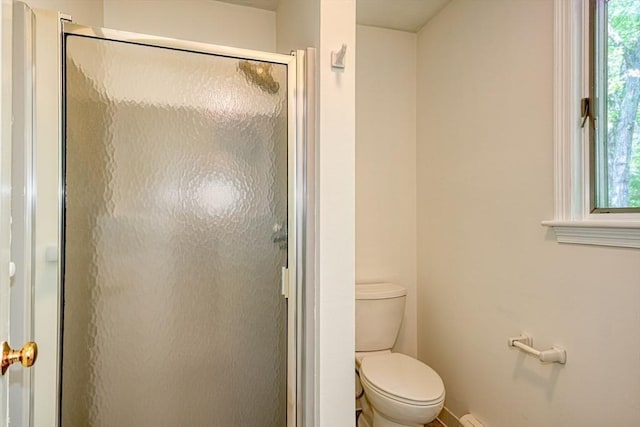 bathroom with toilet, a shower stall, plenty of natural light, and baseboards