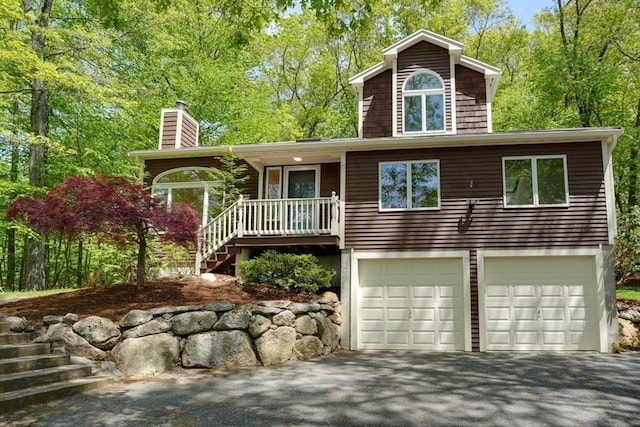 view of front of home with an attached garage, driveway, a chimney, and stairway