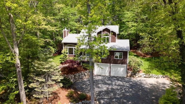 view of front of property with driveway, a garage, a chimney, and a forest view