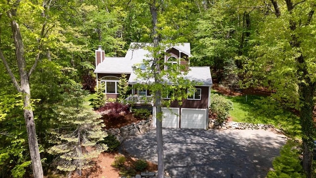 view of front of house with driveway, a garage, a wooded view, and a chimney