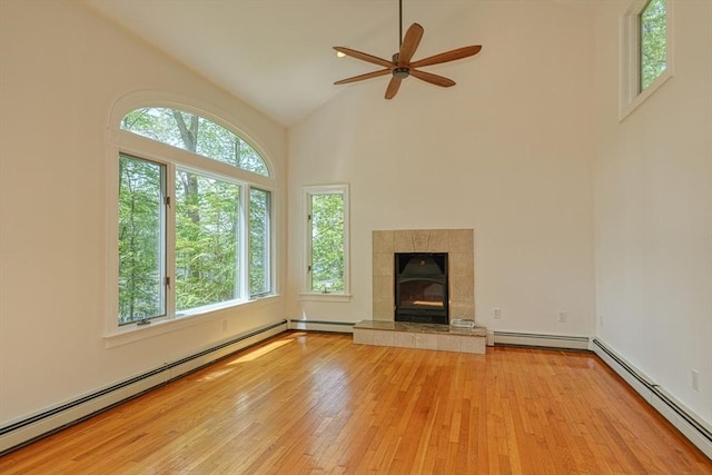 unfurnished living room with a baseboard heating unit, light wood-type flooring, high vaulted ceiling, and plenty of natural light