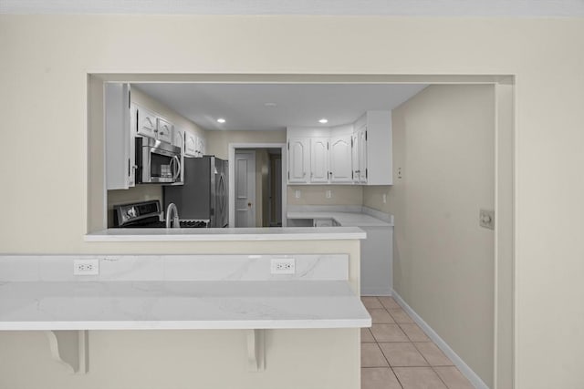 kitchen with appliances with stainless steel finishes, light tile patterned floors, a peninsula, light countertops, and white cabinets