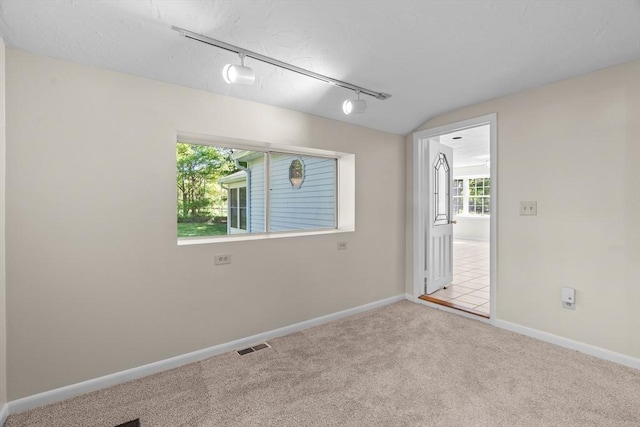 spare room with track lighting, carpet flooring, baseboards, and lofted ceiling
