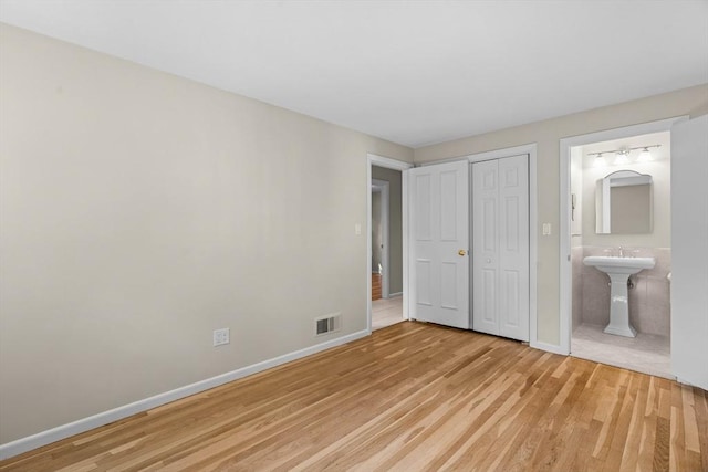 unfurnished bedroom with light wood finished floors, baseboards, connected bathroom, a closet, and a sink