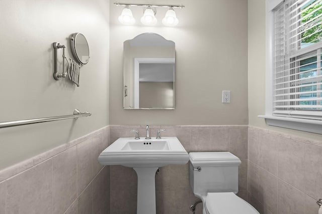 half bath featuring tile walls, toilet, and a wainscoted wall