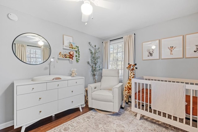 bedroom featuring a nursery area, hardwood / wood-style floors, and ceiling fan