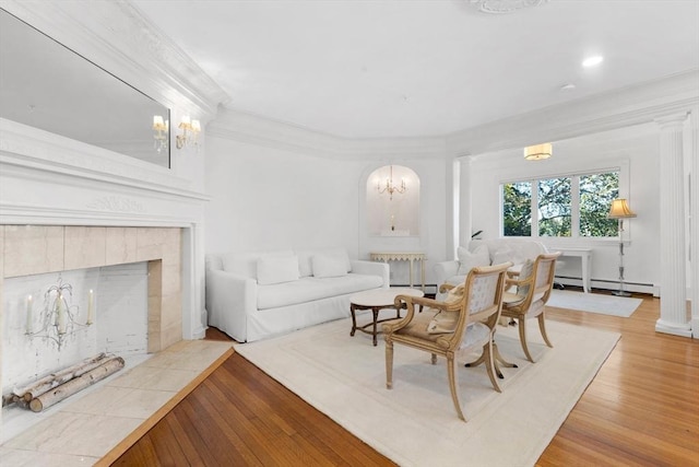 living area with a baseboard heating unit, crown molding, light wood finished floors, and ornate columns