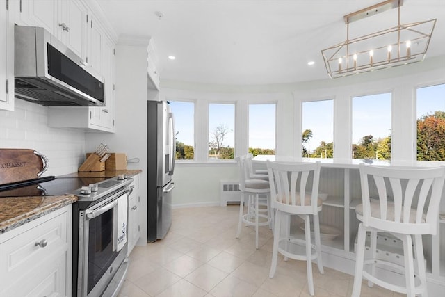 kitchen featuring dark stone counters, radiator, decorative light fixtures, stainless steel appliances, and white cabinetry