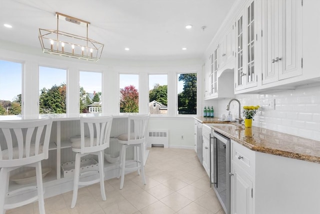 kitchen featuring white cabinets, wine cooler, glass insert cabinets, light stone counters, and pendant lighting