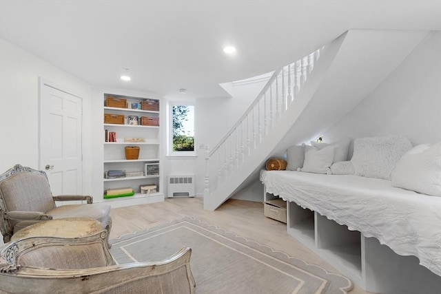 living area with built in shelves, light wood finished floors, recessed lighting, radiator heating unit, and stairs