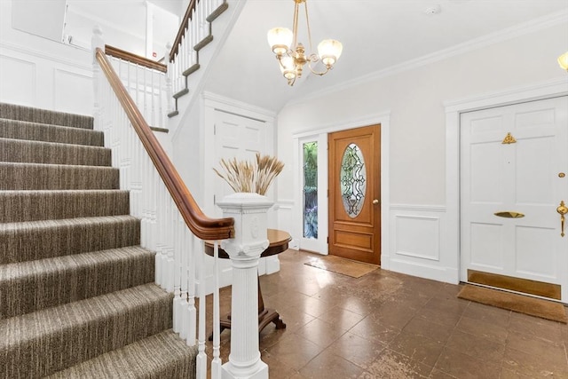 foyer featuring a wainscoted wall, crown molding, a decorative wall, an inviting chandelier, and stairs