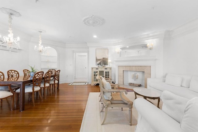 living area with arched walkways, wood finished floors, crown molding, a fireplace, and a chandelier