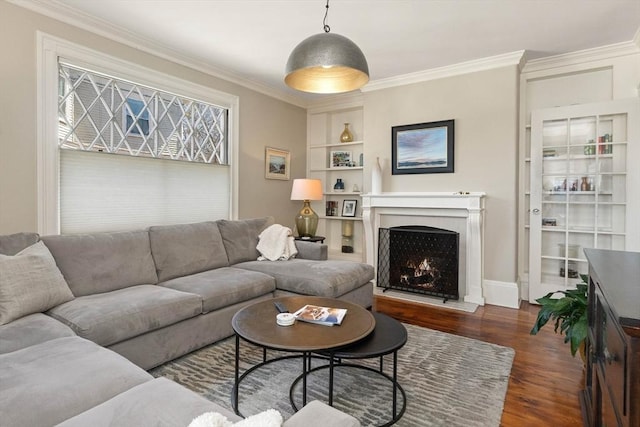 living area featuring baseboards, built in features, ornamental molding, a warm lit fireplace, and wood finished floors