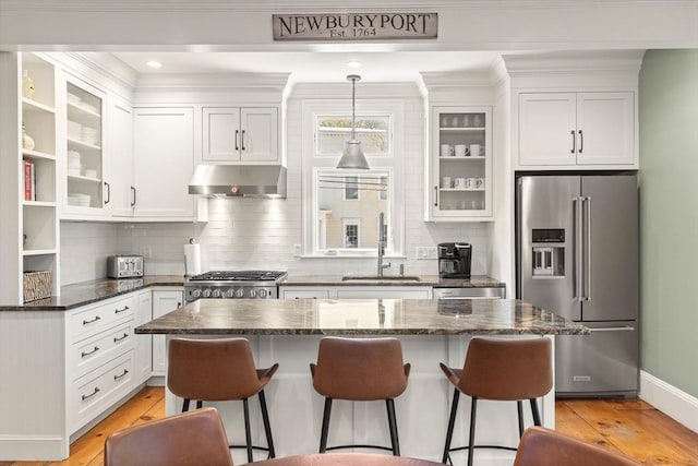 kitchen with under cabinet range hood, high end refrigerator, stove, white cabinetry, and a sink