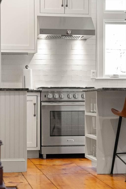 kitchen featuring stainless steel gas stove, white cabinetry, wall chimney range hood, and tasteful backsplash