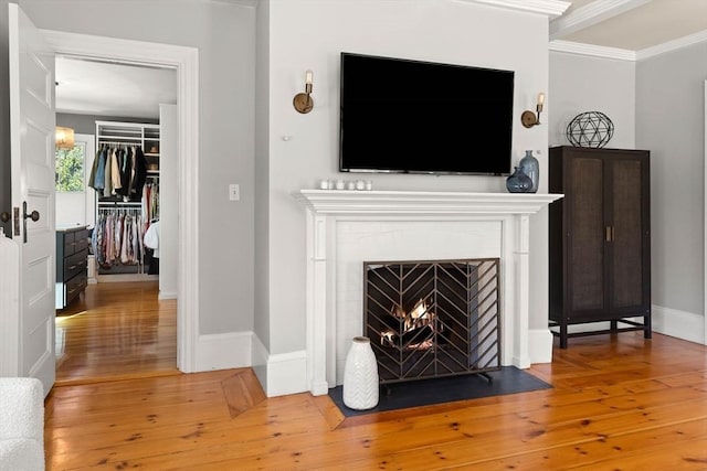 living area with light wood-type flooring, a fireplace with flush hearth, baseboards, and ornamental molding