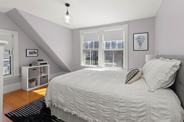 bedroom with vaulted ceiling, baseboards, and wood finished floors
