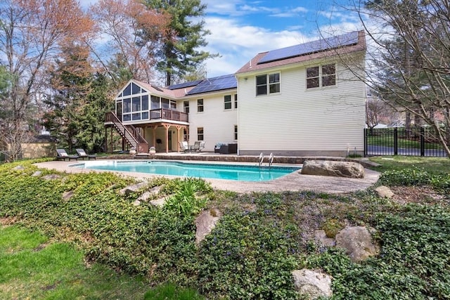 rear view of property with solar panels, an outdoor pool, a sunroom, a patio area, and stairs
