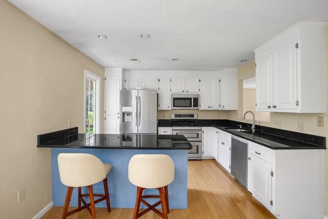 kitchen with white cabinets, appliances with stainless steel finishes, a sink, a breakfast bar area, and a peninsula