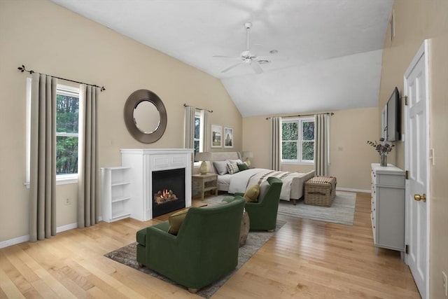 bedroom featuring multiple windows, a warm lit fireplace, and light wood-style flooring