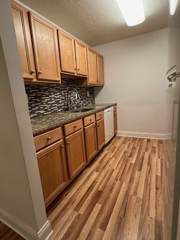 kitchen with backsplash, light wood-style flooring, white dishwasher, a textured ceiling, and a sink