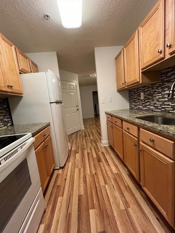 kitchen featuring light wood finished floors, electric range, a sink, a textured ceiling, and backsplash