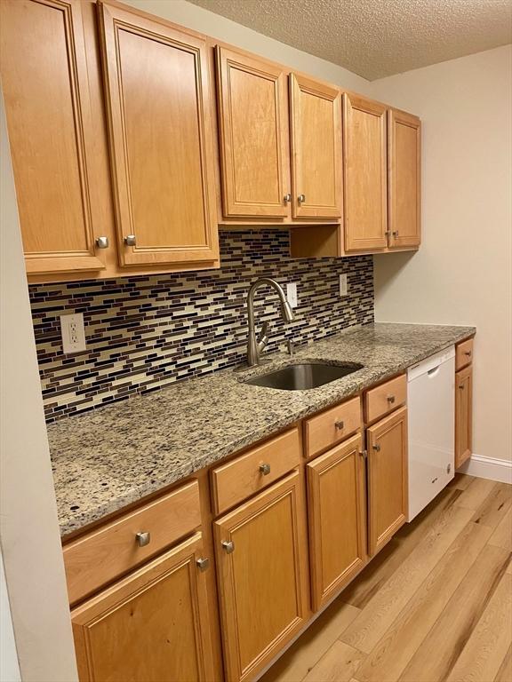 kitchen with light wood-style flooring, a sink, backsplash, white dishwasher, and light stone countertops