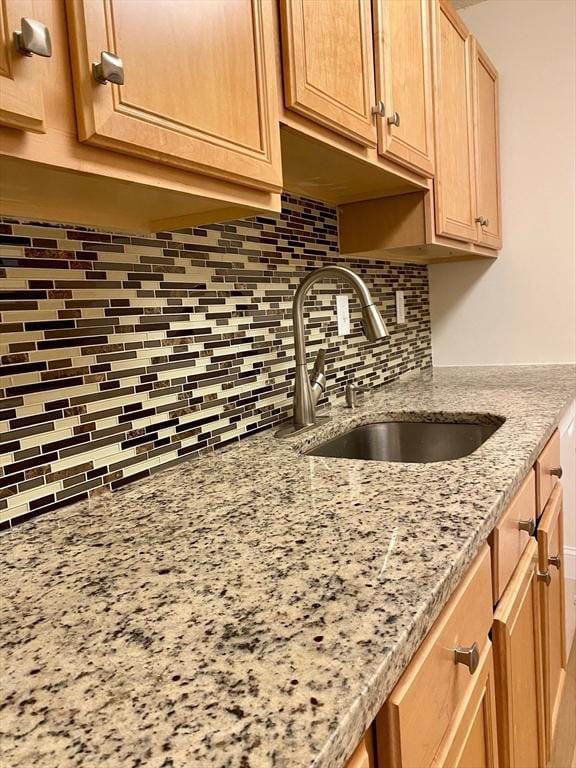 kitchen featuring backsplash, light stone countertops, and a sink