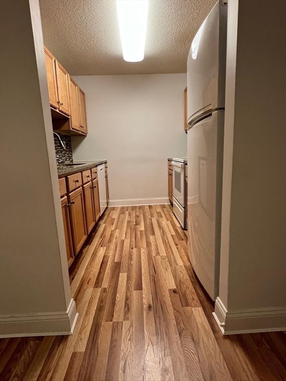 kitchen featuring light wood finished floors, white dishwasher, freestanding refrigerator, a sink, and range with electric cooktop