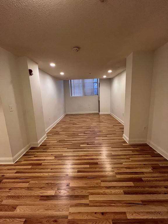 finished below grade area featuring recessed lighting, wood finished floors, baseboards, and a textured ceiling