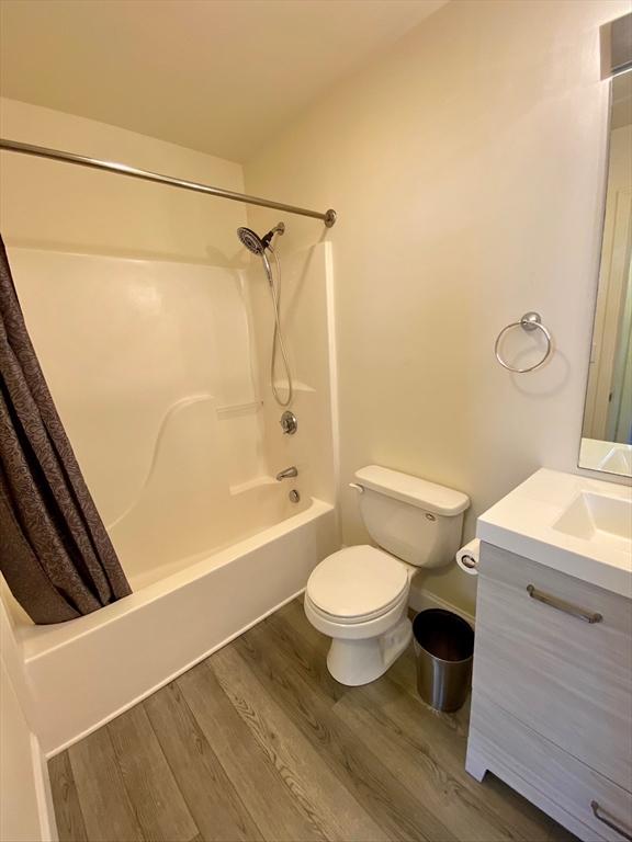 bathroom featuring vanity, toilet, wood finished floors, and shower / tub combo with curtain