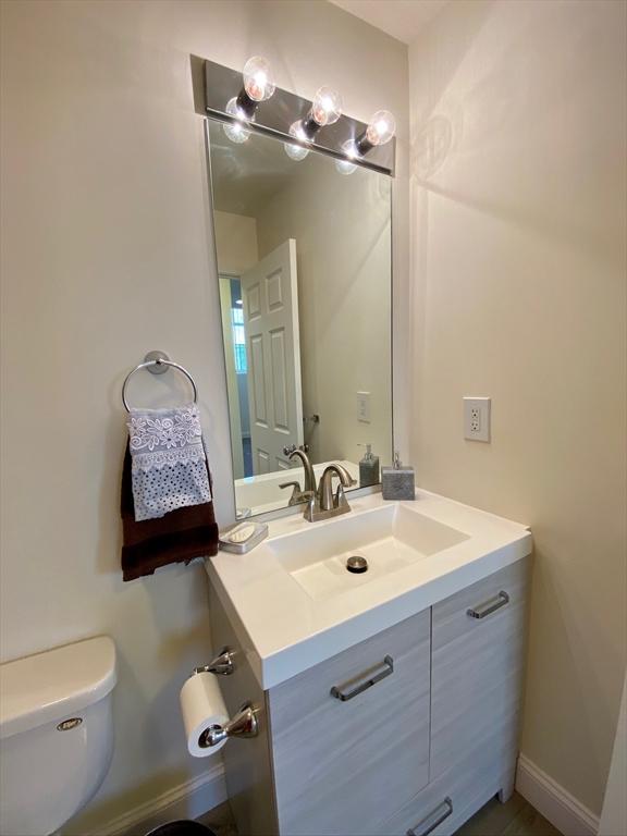 half bath with baseboards, toilet, and vanity