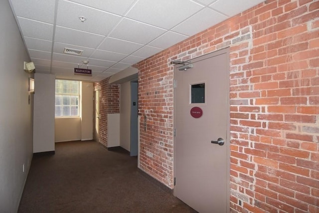 corridor with visible vents, brick wall, a paneled ceiling, and carpet