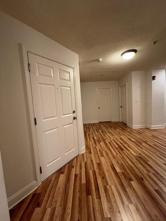 hall featuring baseboards, a textured ceiling, and wood finished floors