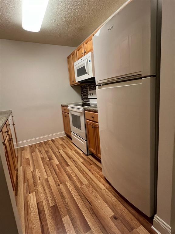 kitchen featuring white appliances, a textured ceiling, light wood-type flooring, and baseboards