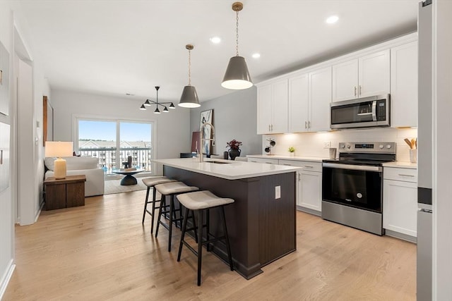 kitchen with appliances with stainless steel finishes, a kitchen breakfast bar, an island with sink, open floor plan, and decorative backsplash