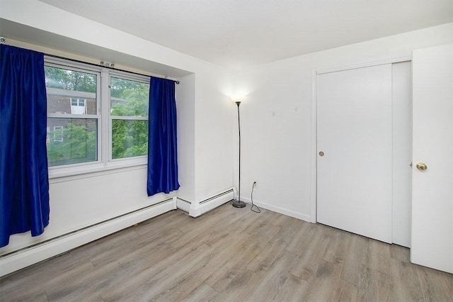 unfurnished bedroom with a closet, wood finished floors, and a baseboard heating unit