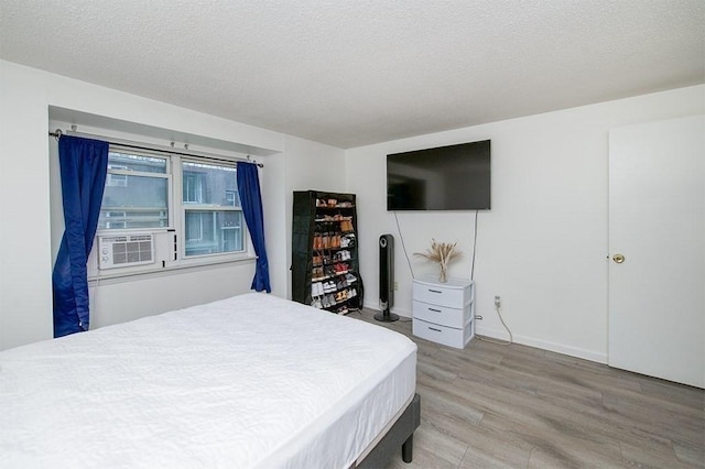 bedroom featuring baseboards, cooling unit, light wood-style floors, and a textured ceiling