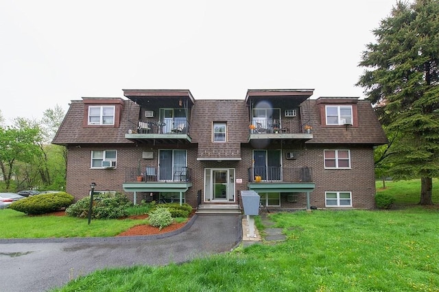 townhome / multi-family property featuring a front yard, a shingled roof, brick siding, and mansard roof