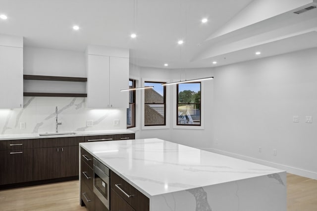 kitchen with a kitchen island, stainless steel microwave, sink, and white cabinetry