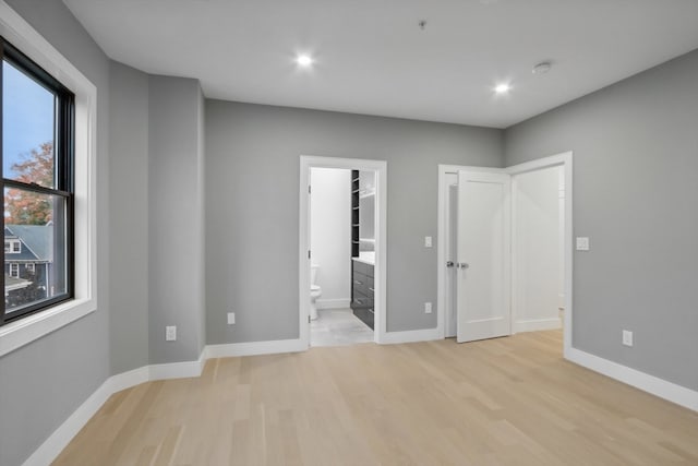 unfurnished bedroom featuring connected bathroom, light hardwood / wood-style floors, and a walk in closet