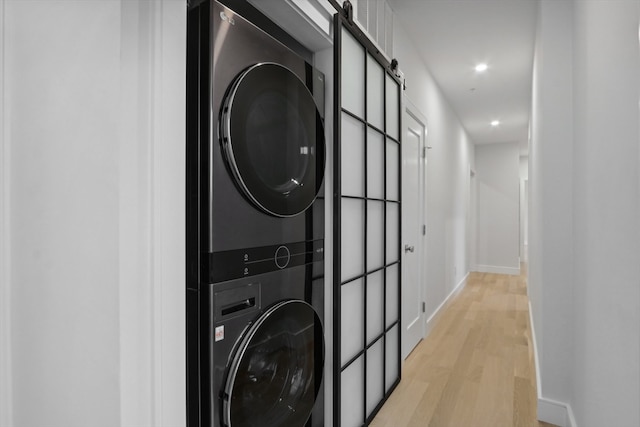 clothes washing area with a barn door, stacked washer and dryer, and light wood-type flooring