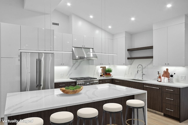 kitchen with dark brown cabinetry, a kitchen island, appliances with stainless steel finishes, a breakfast bar area, and light wood-type flooring