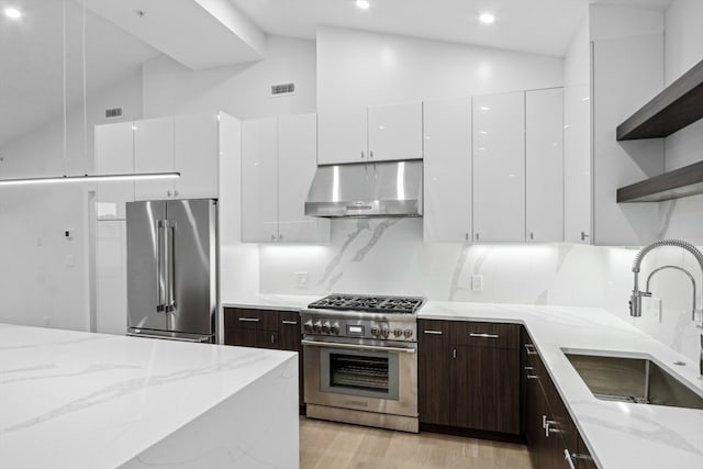 kitchen featuring light stone counters, white cabinets, high end appliances, and high vaulted ceiling