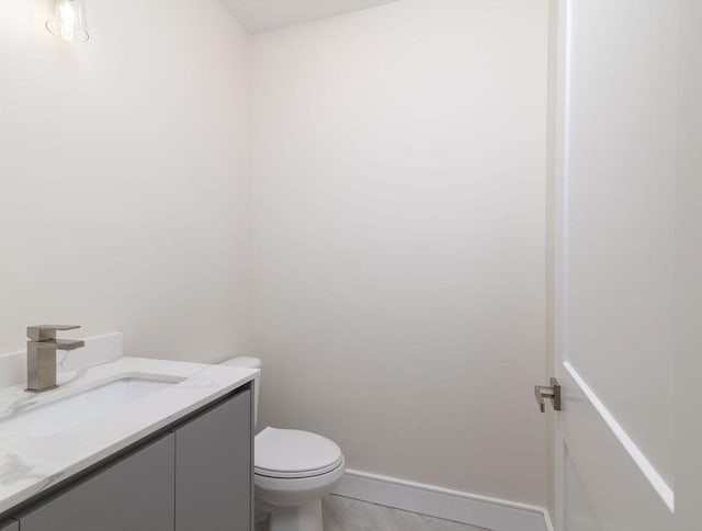 bathroom with toilet, vanity, baseboards, and wood finished floors