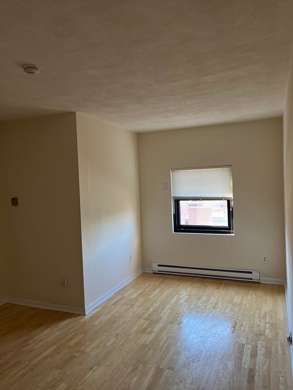 spare room with baseboard heating and light hardwood / wood-style floors