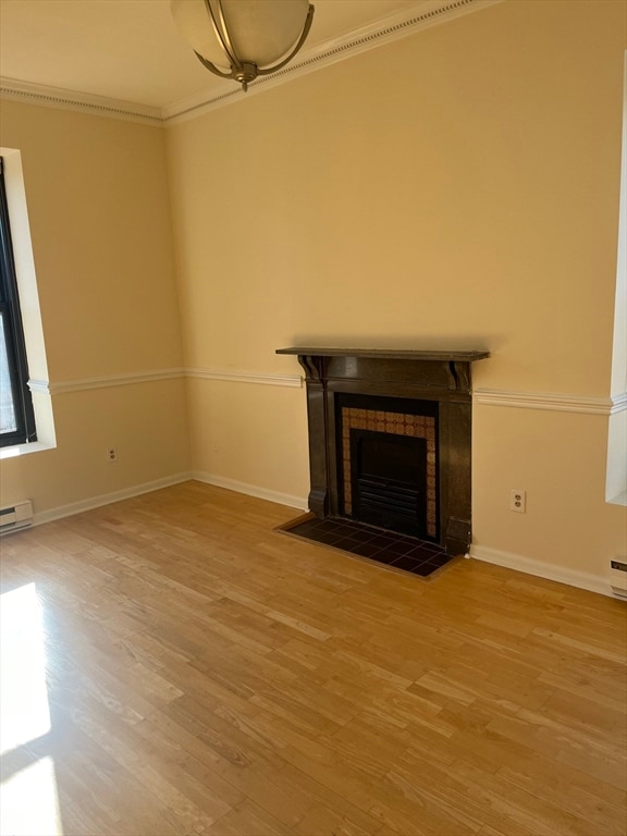 unfurnished living room with wood-type flooring, ornamental molding, and a tiled fireplace