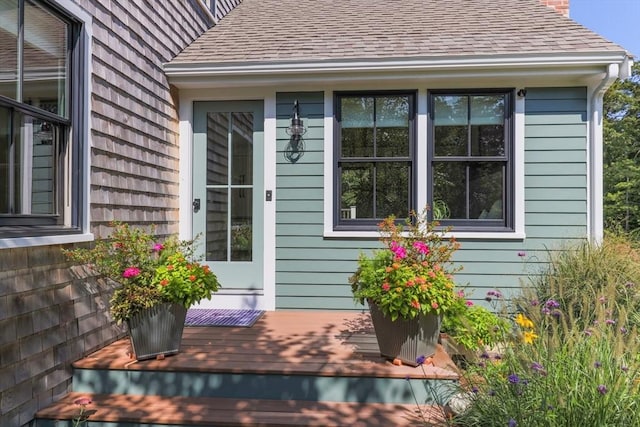 doorway to property featuring a deck and a shingled roof