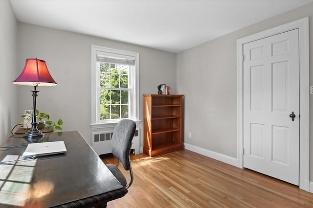 office area with baseboards, radiator heating unit, and light wood-style flooring